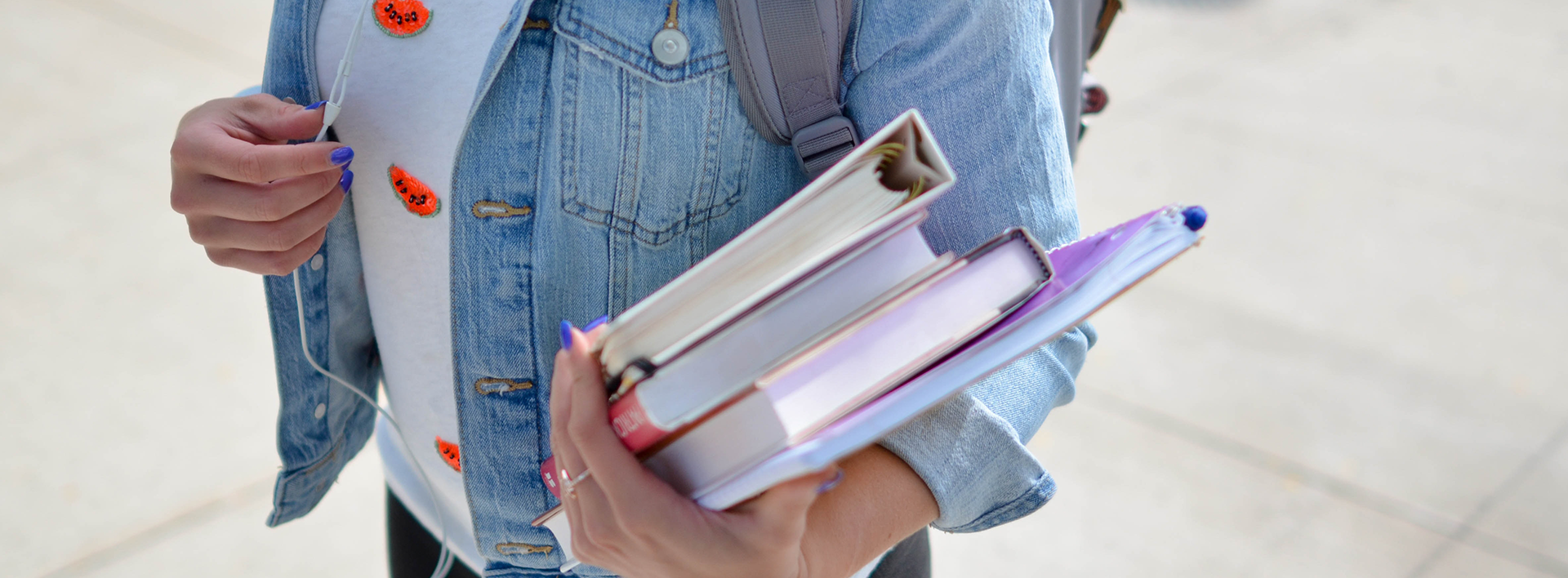 A student wearing a denim jacket and holding books and a folder.