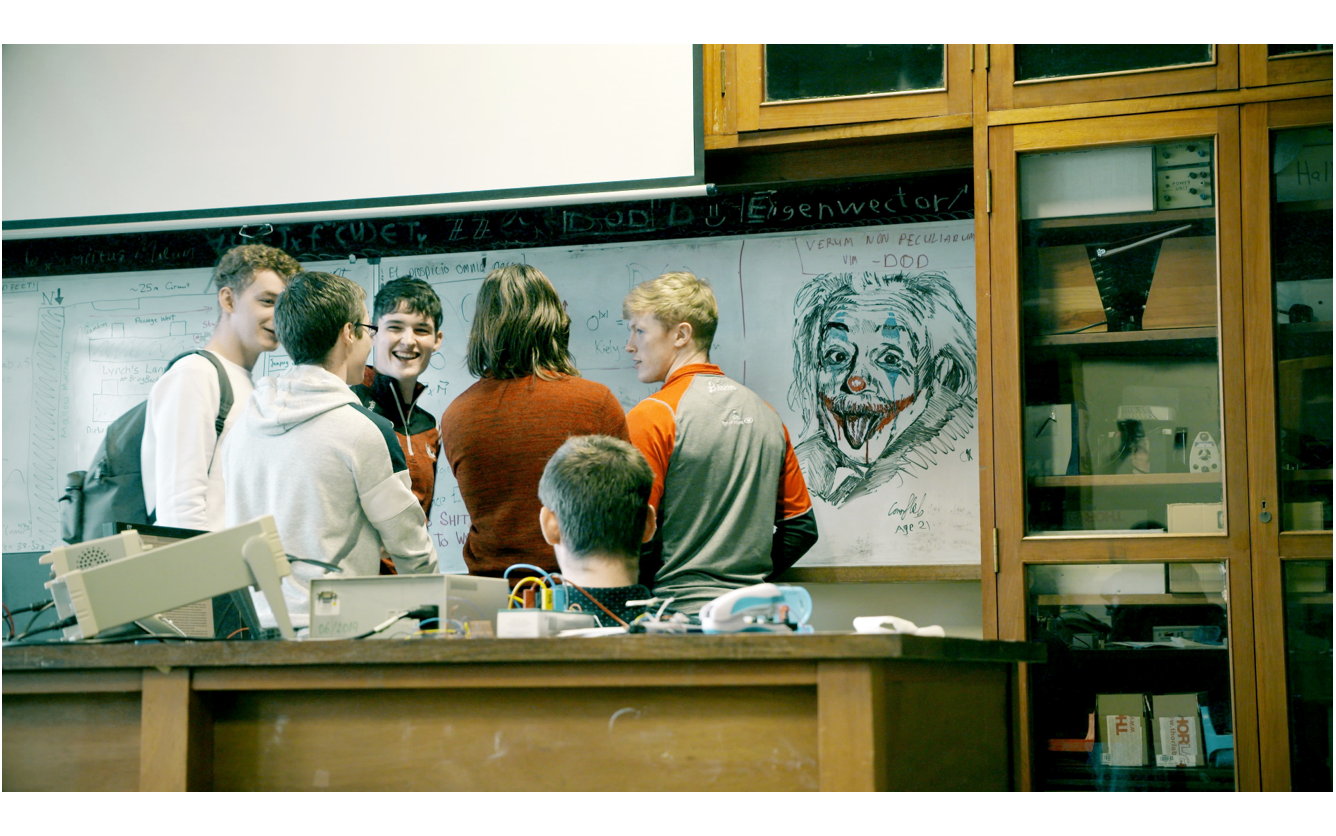 Students in lab at whiteboard chatting with image and text on board