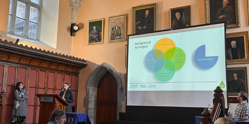 Two women standing by a podium with a large screen in the background Two women standing by a podium with a large screen in the background