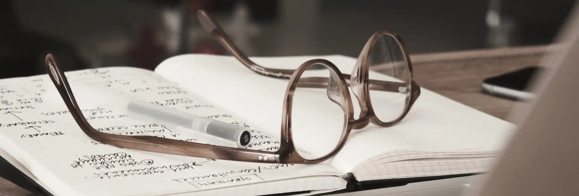 A pair of glasses rests on the open pages of a note book.