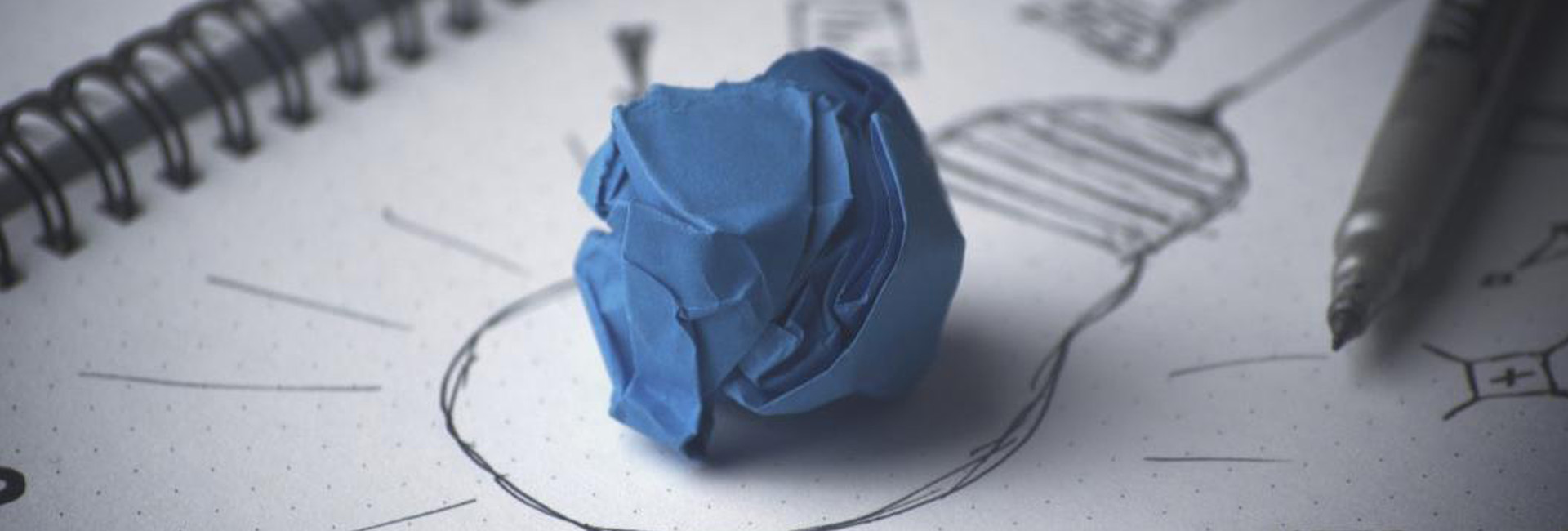 a wadded up piece of blue paper on top of a white sheet of paper with a lightbulb drawn on it in black ink
