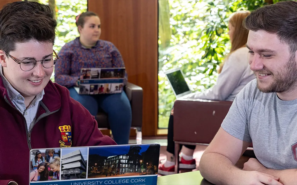 Two students looking at an open laptop in the Boole Library, smiling.