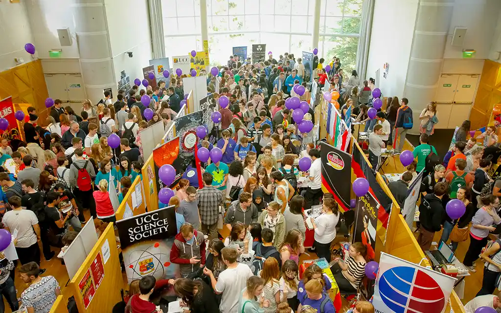 wide pan overhead shot of a busy room with multiple stands displaying all of ucc societies and their members